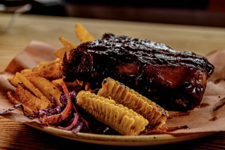 Henry’s smoked pork ribs plated with fries and charred corn as a serving suggestion